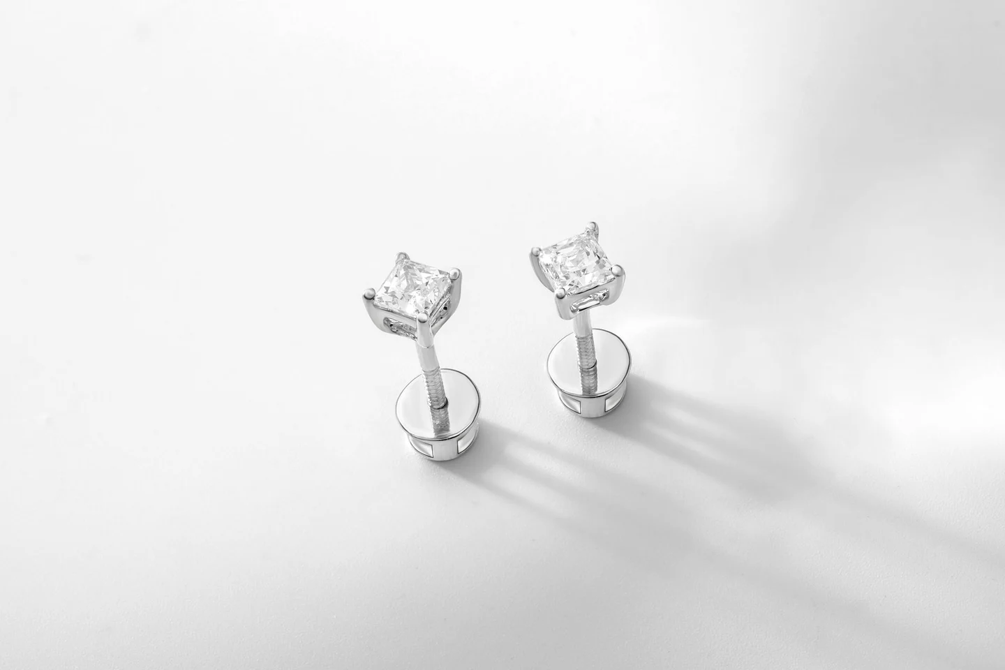 A pair of diamond stud earrings casting soft shadows on a white surface