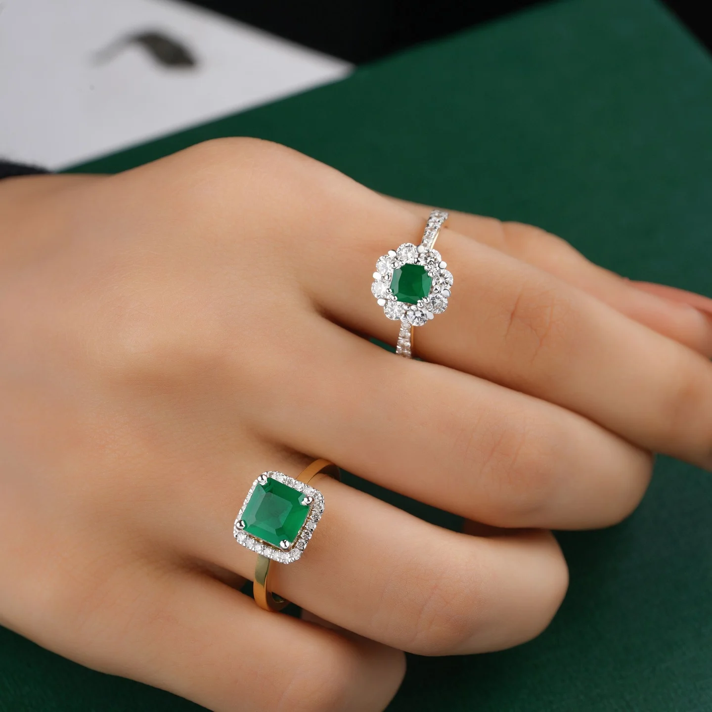 Close photograph of emerald and diamond rings worn on a hand