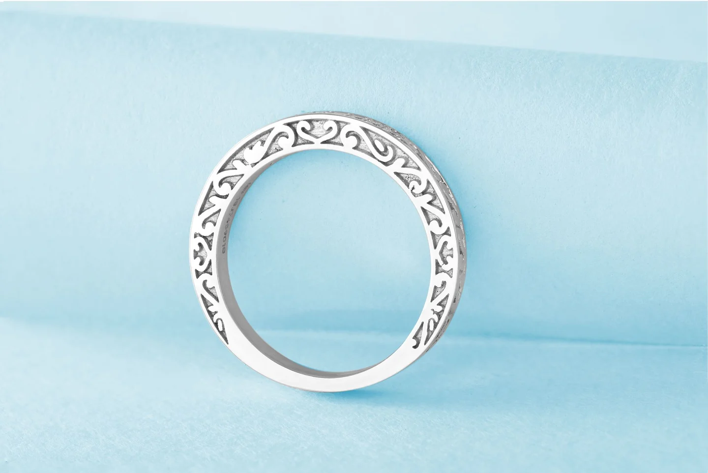 Side view of a silver-colored ring showing its openwork setting on pale blue paper